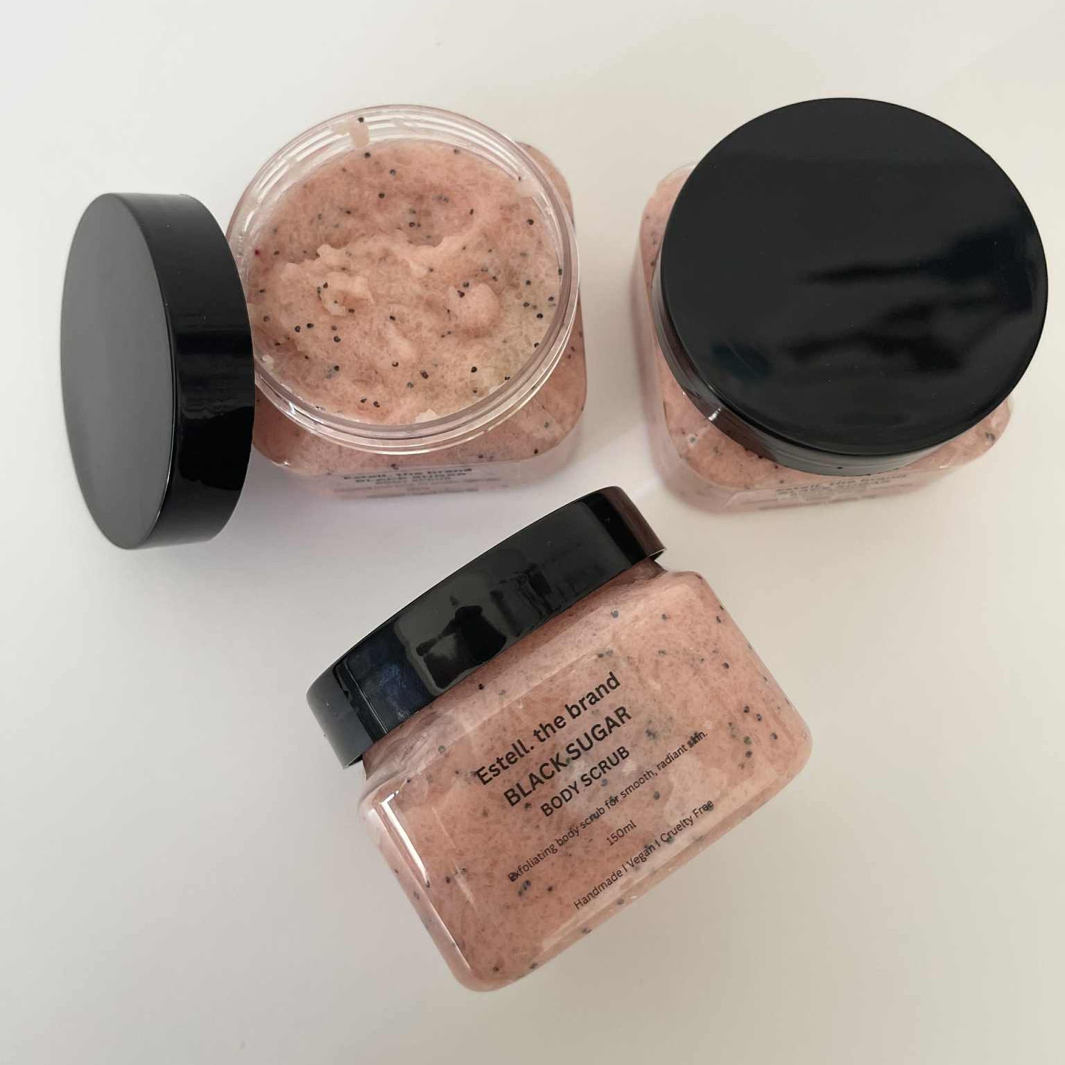 Three jars of black sugar scrub with black lids on a white background