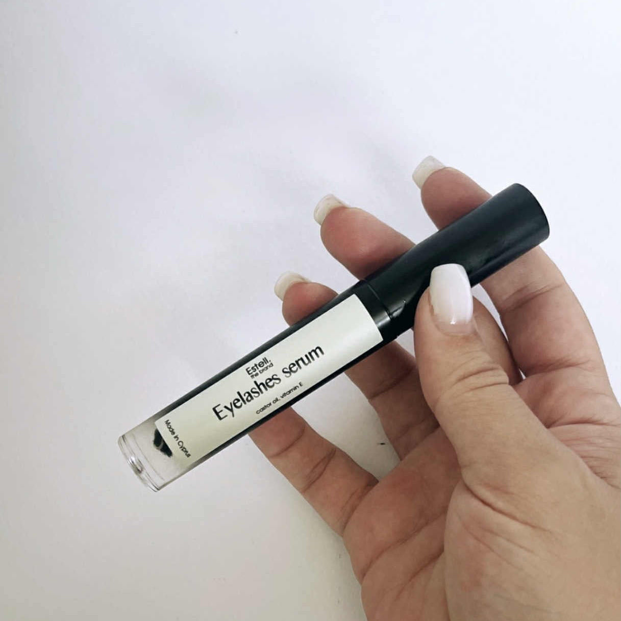 Hand holding an eyelash serum with a white background