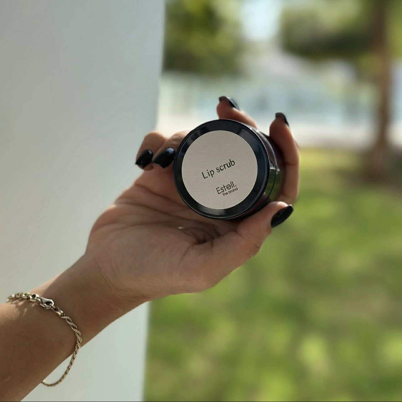 Hand holding a jar of lip scrub with a blurred outdoor background