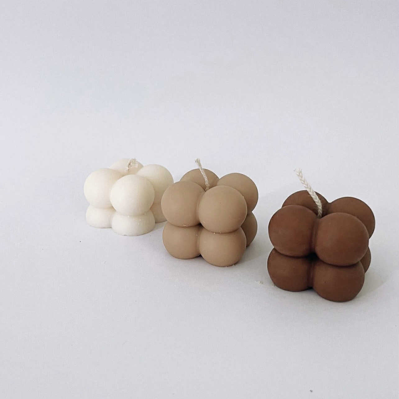 Three candle sets shaped like stacked spheres in white, beige, and brown on a light gray background.