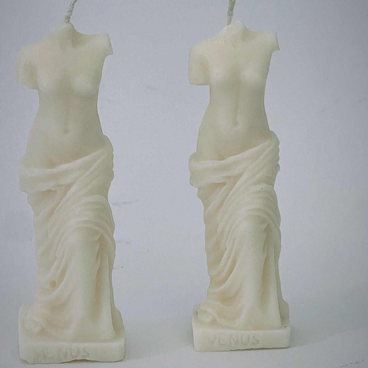 Two candle sculptures shaped like classical statues on a white background