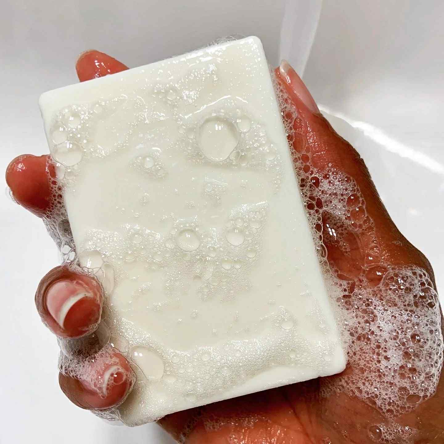 Hand holding a bar of soap with lather on a white background