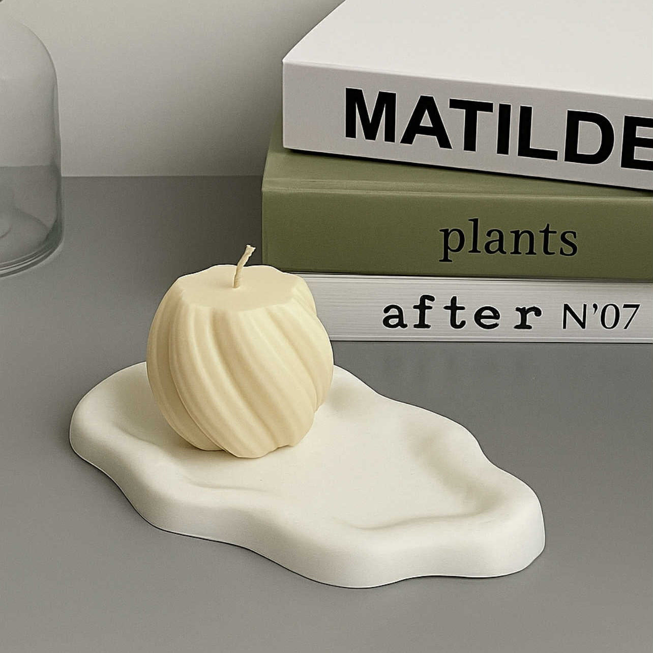 White ceramic dish with a small white sculpture on a gray surface with books in the background.