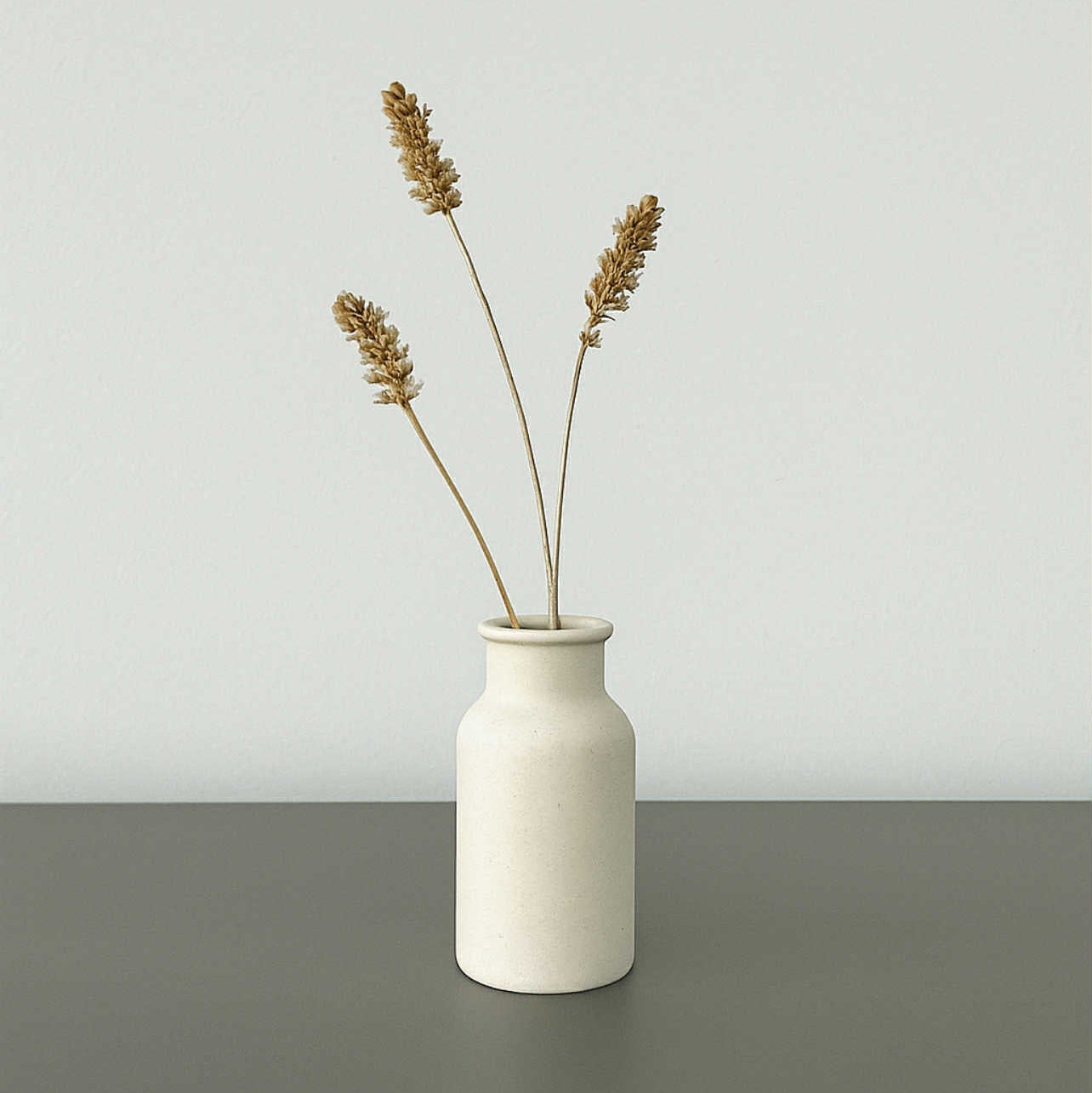White ceramic vase with dried plants on a gray surface and light gray background